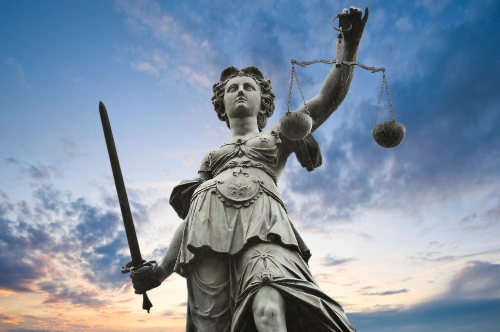 Statue of Lady Justice holding a sword and scales against a sunset sky
